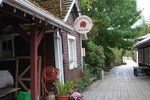 Narrow boardwalk between rustic wooden buildings with potted flowers and trees in the background